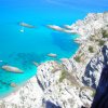 Vista di una scogliera con mare turchese e barche ancorate.