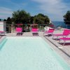 Piscina con lettini rosa e cielo sereno.