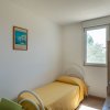 Letto singolo con copriletto giallo sotto una finestra, quadro alla parete.