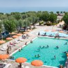 Piscina affollata con ombrelloni arancioni e vista sul mare.