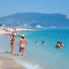Persone in mare e sulla spiaggia, montagne sullo sfondo.