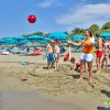 Persone giocano a palla su una spiaggia con ombrelloni blu.