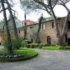 Ampio viale alberato con un edificio in pietra e prato fiorito.