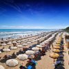 Spiaggia con file di ombrelloni e lettini, mare calmo e cielo blu.