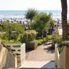 Scalinata verso una spiaggia con persone e ombrelloni blu bianchi, alberi e cespugli.