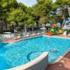 Piscina con giocattoli galleggianti, circondata da alberi e sedie a sdraio.
