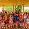 Gruppo di bambini con mascotte verde sorridente.