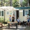 Gruppo di amici fuori da una roulotte, intorno a un tavolo all'aperto, con barbecue e ombrellone.