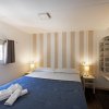 Camera con letto matrimoniale, pareti a strisce beige, due lampade e finestra laterale.