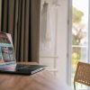 Laptop su scrivania accanto a finestra aperta.