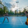 Due ragazzi giocano a basket su un campo esterno.