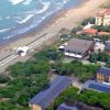 Vista aerea di una spiaggia sabbiosa con file di ombrelloni e edifici circondati da vegetazione.
