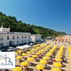 Spiaggia con ombrelloni gialli di fronte a hotel bianco.