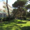 Edificio bianco con balconi verdi, alberi e prato curato.