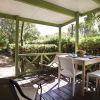 Veranda in legno con tavolo, sedie bianche e vegetazione circostante.