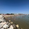Mare con bagnanti e un lungo molo di rocce. Spiaggia sullo sfondo.