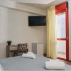 Camera con letto, TV a parete, scrivania, finestra con tenda chiara e porta rossa.