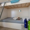 Letto a castello con lenzuola grigie, orsetto di peluche e due bottiglie riutilizzabili su tavolo.