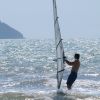 Una persona fa windsurf tra le onde di fronte a un paesaggio collinare.