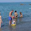 Persone in acqua lungo una spiaggia, tra cui un uomo e un bambino con un salvagente.