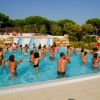 Persone che fanno acquagym in piscina all'aperto, con alberi sullo sfondo.