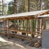 Struttura coperta in legno con tavoli lunghi tra gli alberi.